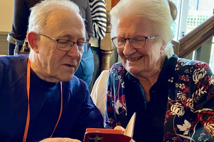 A older gentleman with glasses helping an older lady, also with glasses, with a smart phone