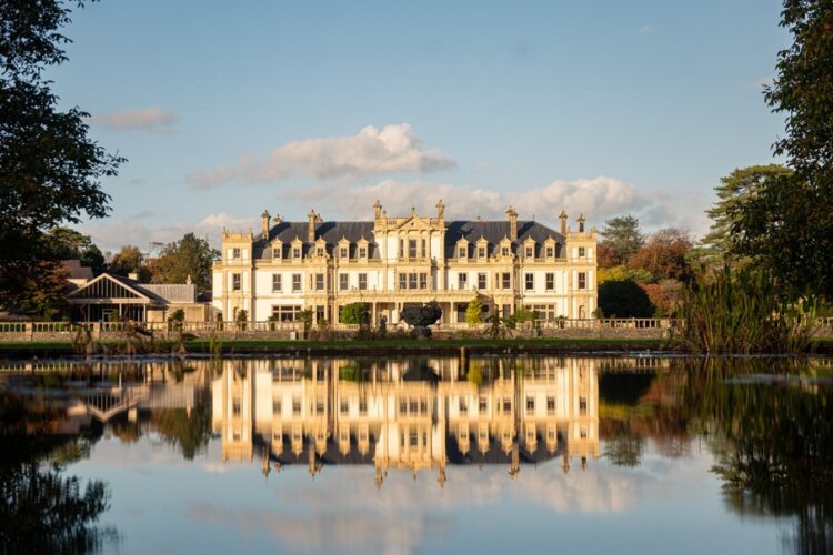 A beautiful light coloured mansion with its reflection in a large lake in front of it