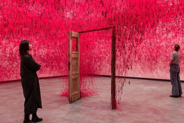 Two people stand on either side of an open door in Chiharu Shiota: Threads of Life