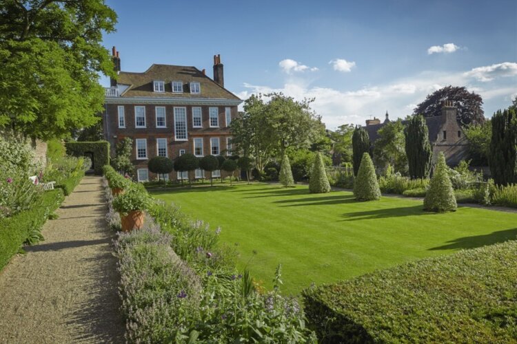 A large and well manicured lawn sit in front of a tall country house with lots of windows