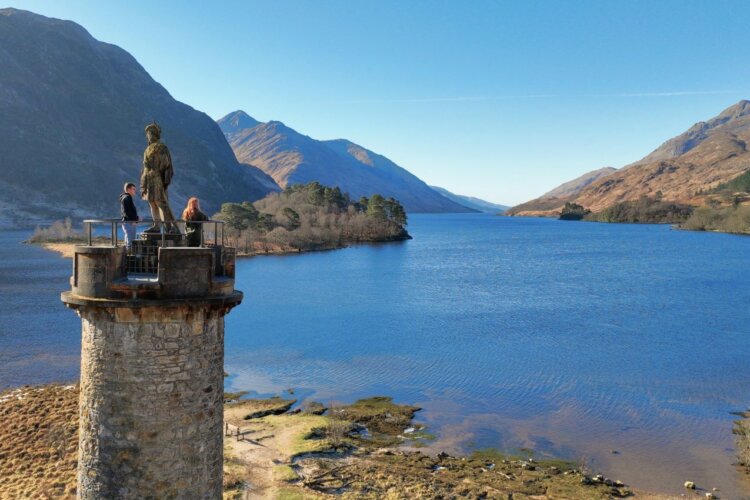 Image shows two people at the top of Glenfinnan Monument, overlooking Loch Shiel.