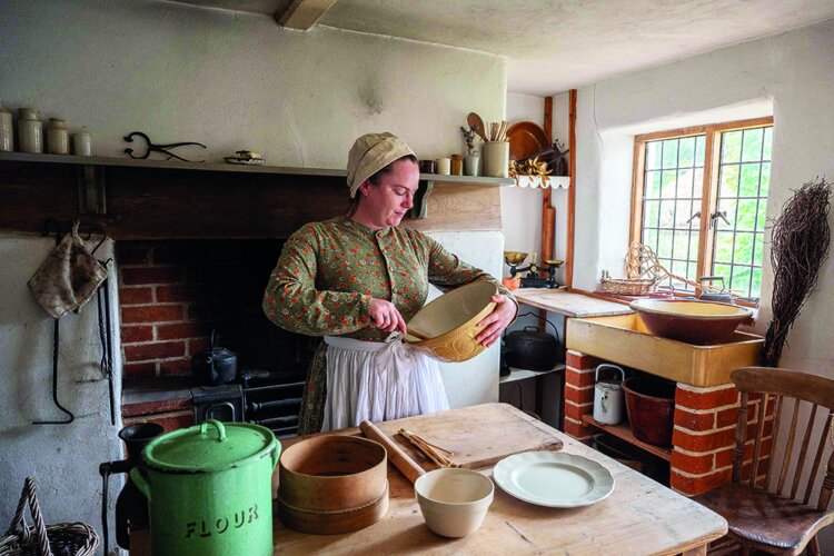 Woman dressed in Victorian clothing cooking in a Victorian kitchen.