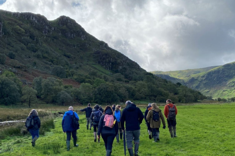 A group of adults walking alongside a river at Wild Haweswater with hills rising up in the background