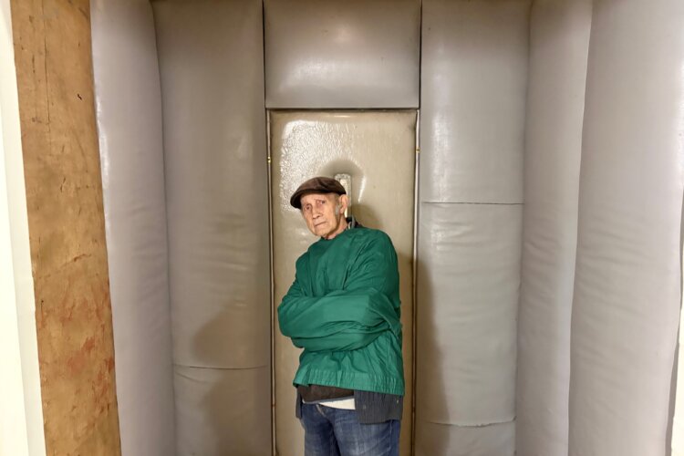 man wearing straitjacket, item of clothing, used for mental illness in the past, pictured in a mock up of a padded cell room
