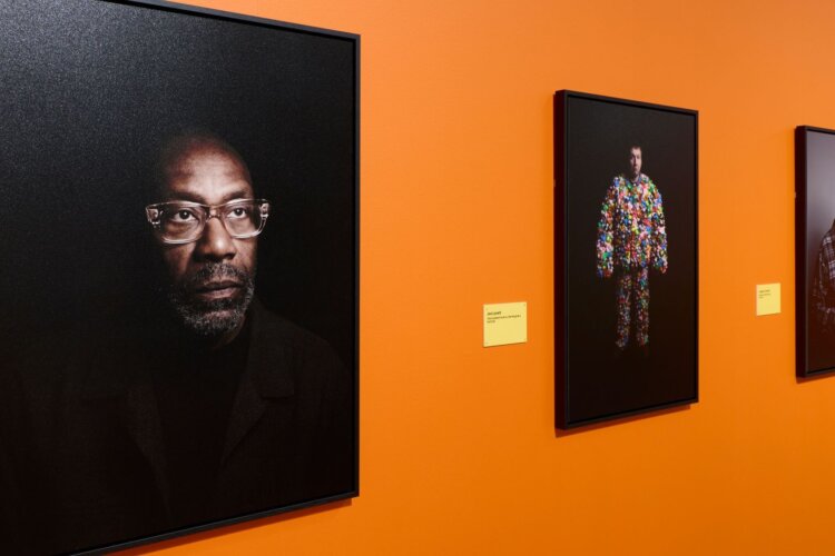 Portraits of Lenny Henry, Joe Lycett and Jasper Carrot on a bright orange wall.