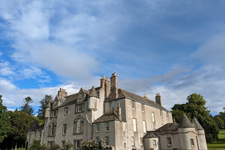 A white country house at the end of a gravel drive, surrounded by lawn and trees
