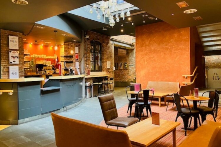 A picture of a bar setting with a counter with chairs and tables in front.