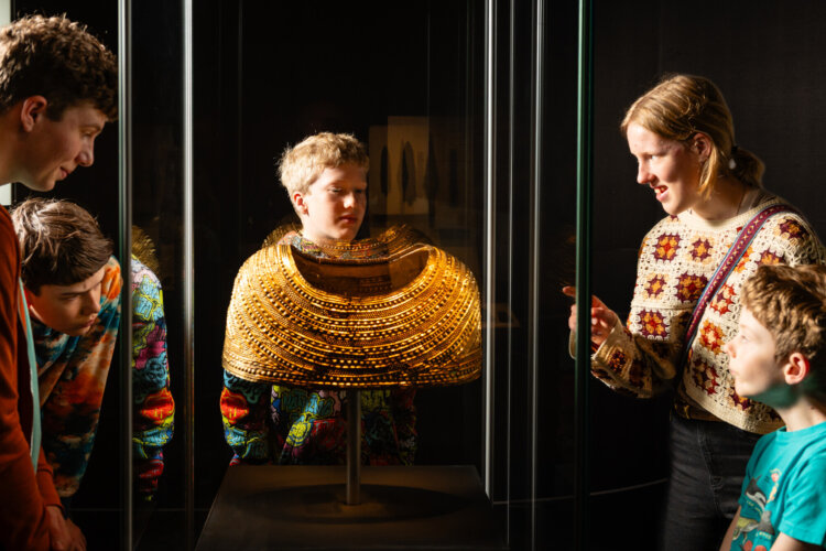 Children looking at a ancient gold cape with patterns stamped into it, in a museum display case