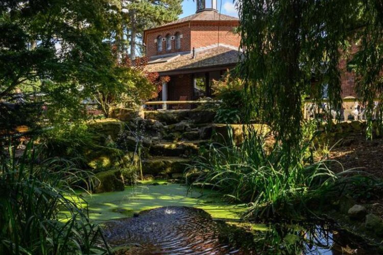 The side of the Memorial Hall viewed through trees in our Memorial Garden and pond to the forefront.