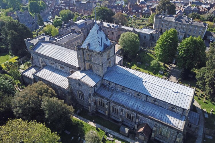 Aerial view of a large stone church with a tower and spiral, amongst the trees and other buildings.