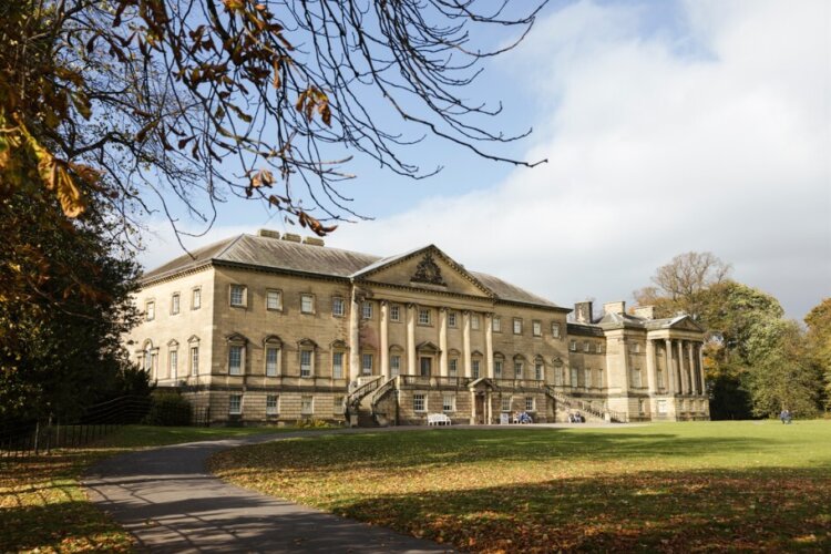 A sprawling mansion with many columns overlooking a mature garden