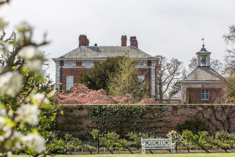 An old house and bell tower behind a walled garden with a white bench