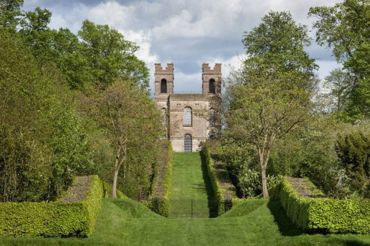 The front of an old castle amongst a beautifully manicured lawn and hedges