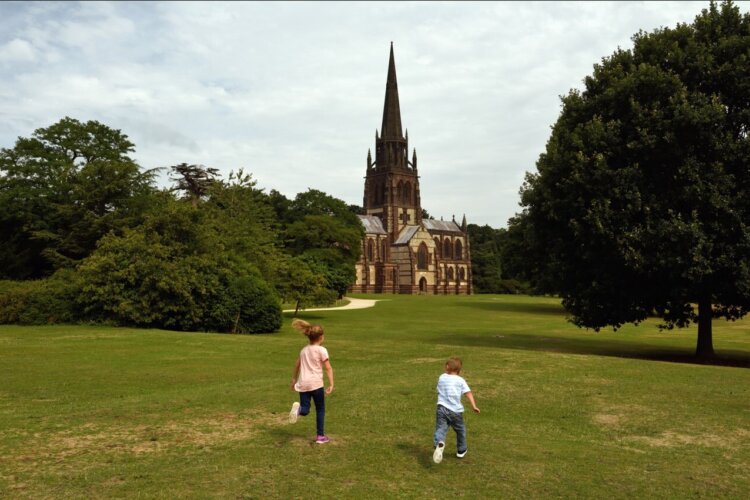 two young children are running in a green field with a big church in the background