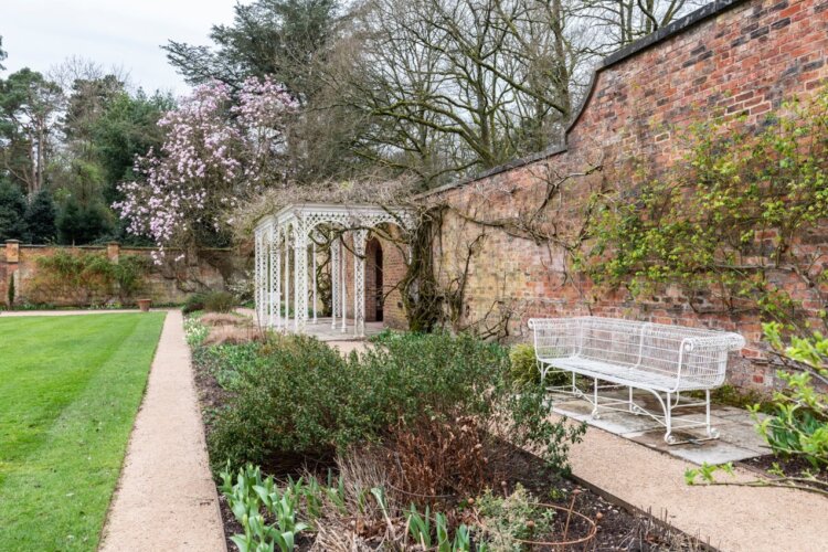 Inside a walled garden sit a white bench and pergola