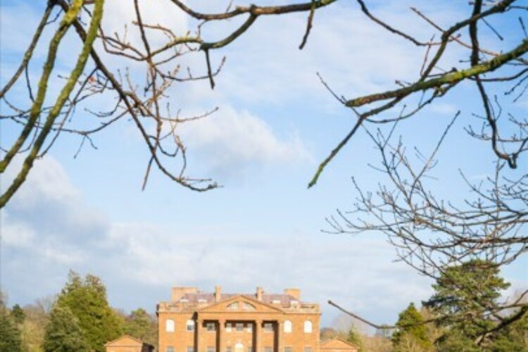 A large mansion sits in the foreground of a big garden