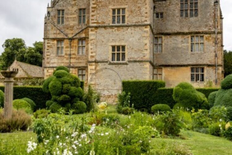 A well manicured garden sits in front of an old house with castle like features