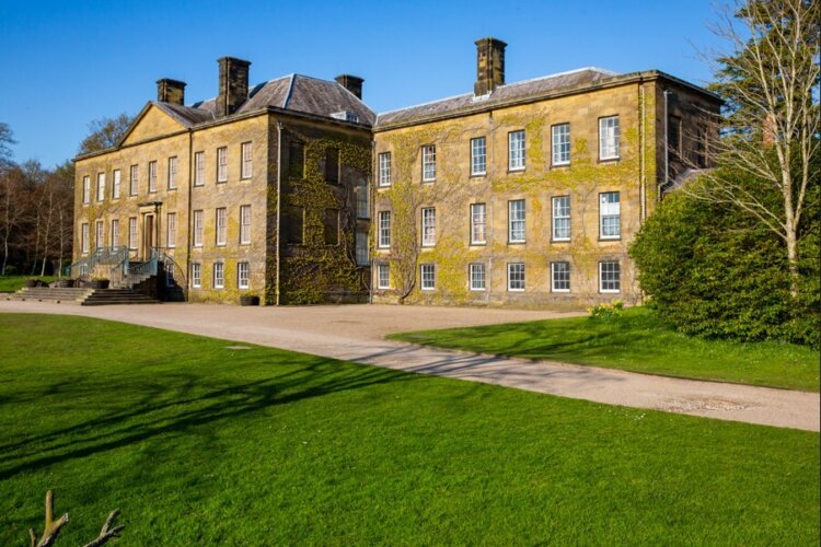 A light coloured old country house with many windows and a well kept garden
