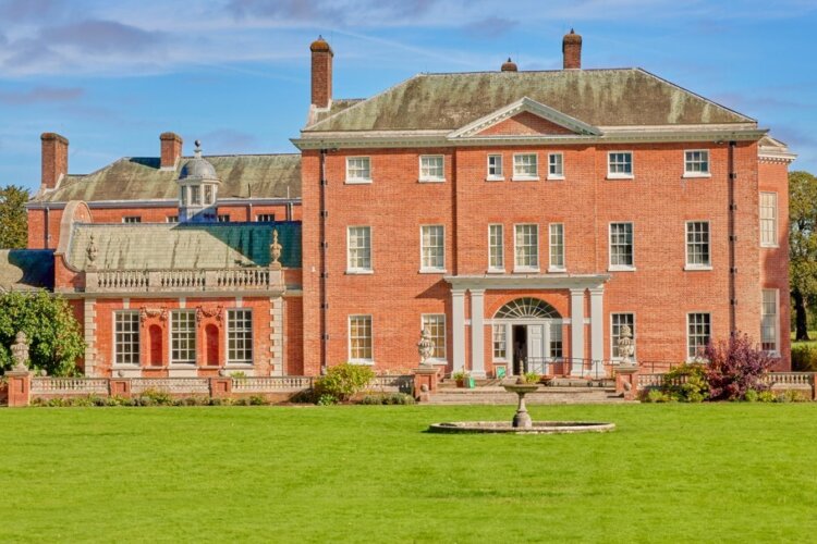 A large red brick house with lots of windows and a garden with a stone water feature