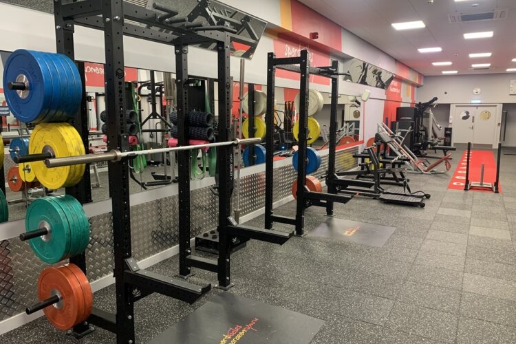 A mirrored wall with blue, green, yellow and red weights in front of it and grey mats with other gym equipment