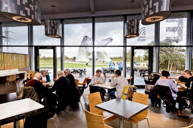 A picture of the Helix Visitor Centre Café with groups of people sitting at tables with the Kelpies in the background.
