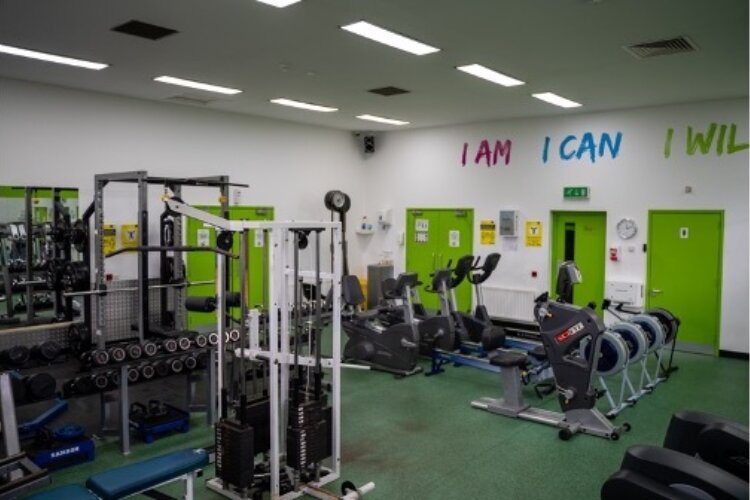Gym equipment, such as weights, running machines and cross trainers are in a room painted white and green with the words 'I AM, I CAN, I WILL' on the wall.