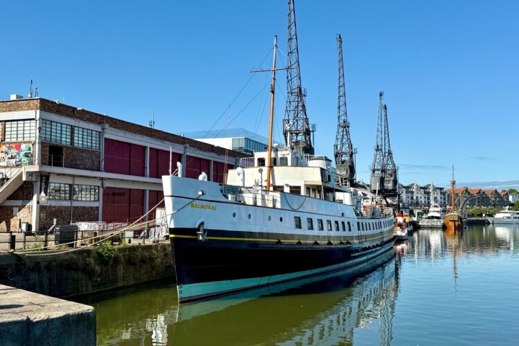 A large white motor ship berthed in the water alongside the quayside and its cranes