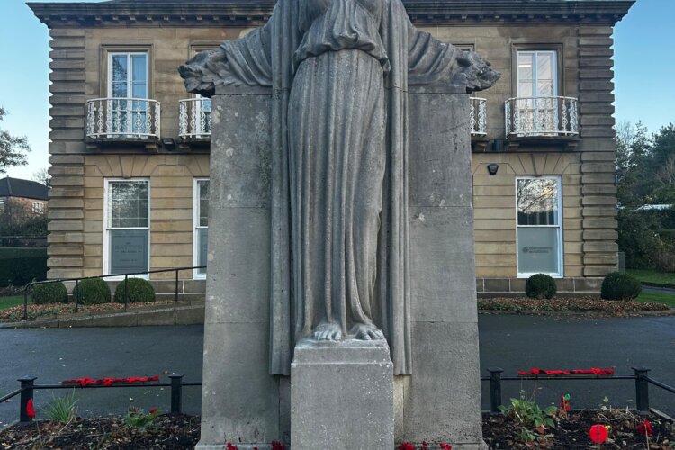 A grey statue of a woman stands in front of a building with poppies in front of her