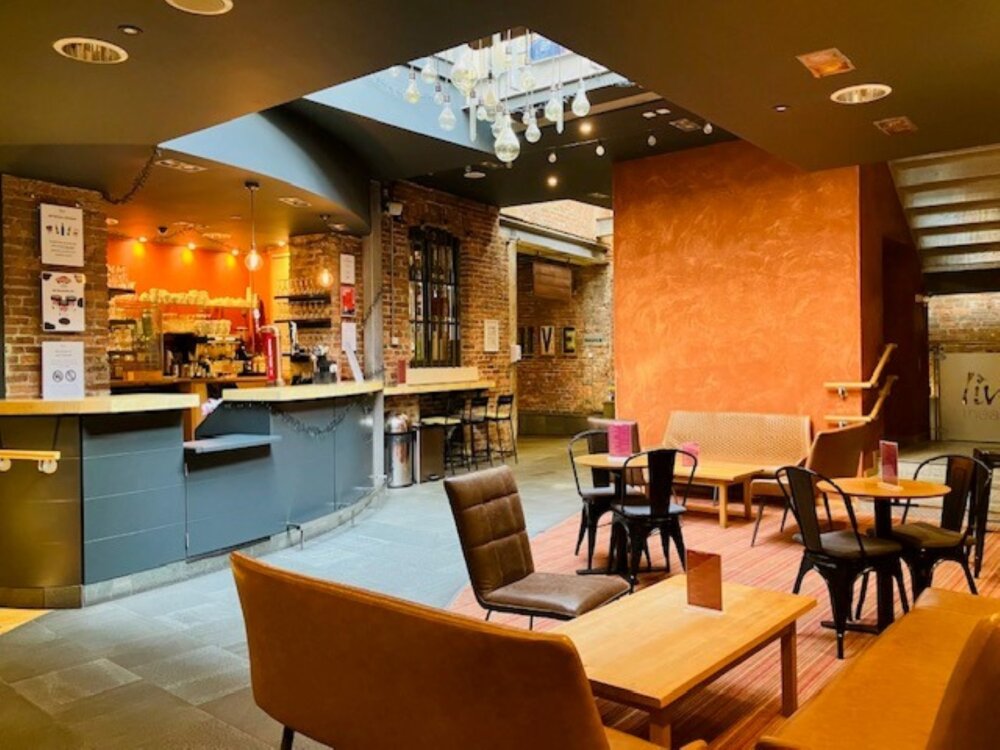 A picture of a bar setting with a counter with chairs and tables in front.