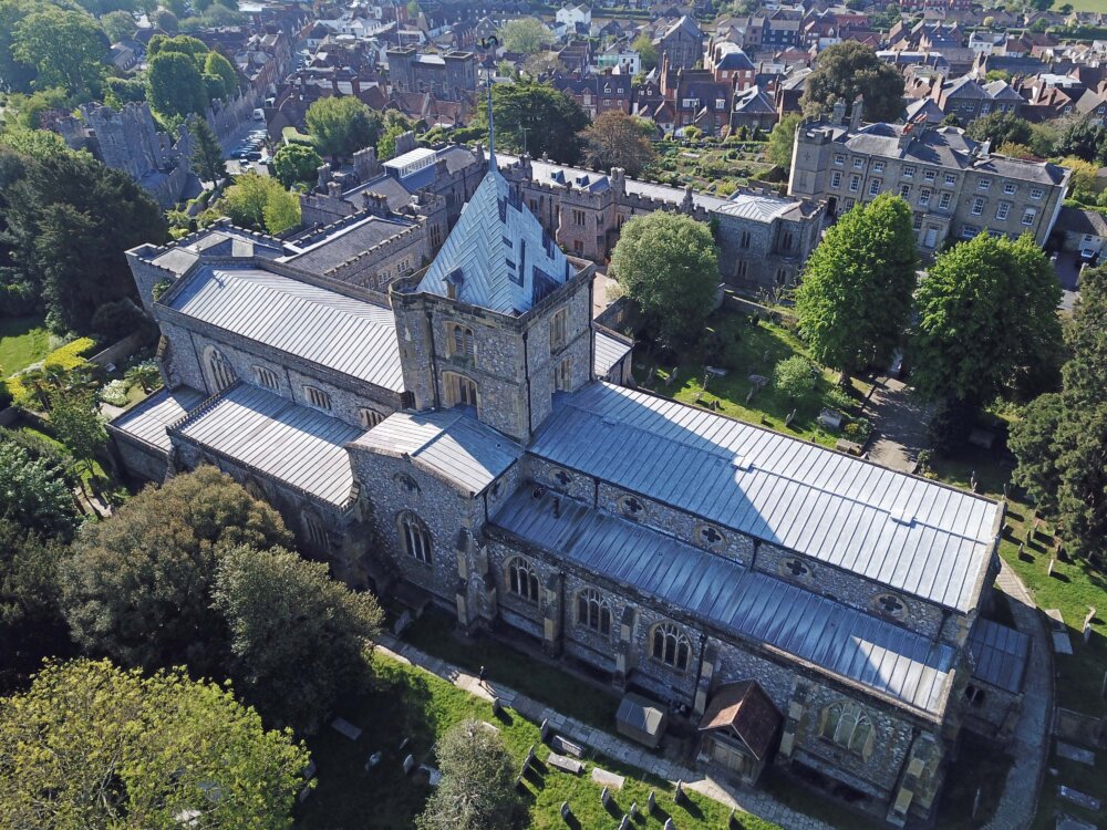 Aerial view of a large stone church with a tower and spiral, amongst the trees and other buildings.